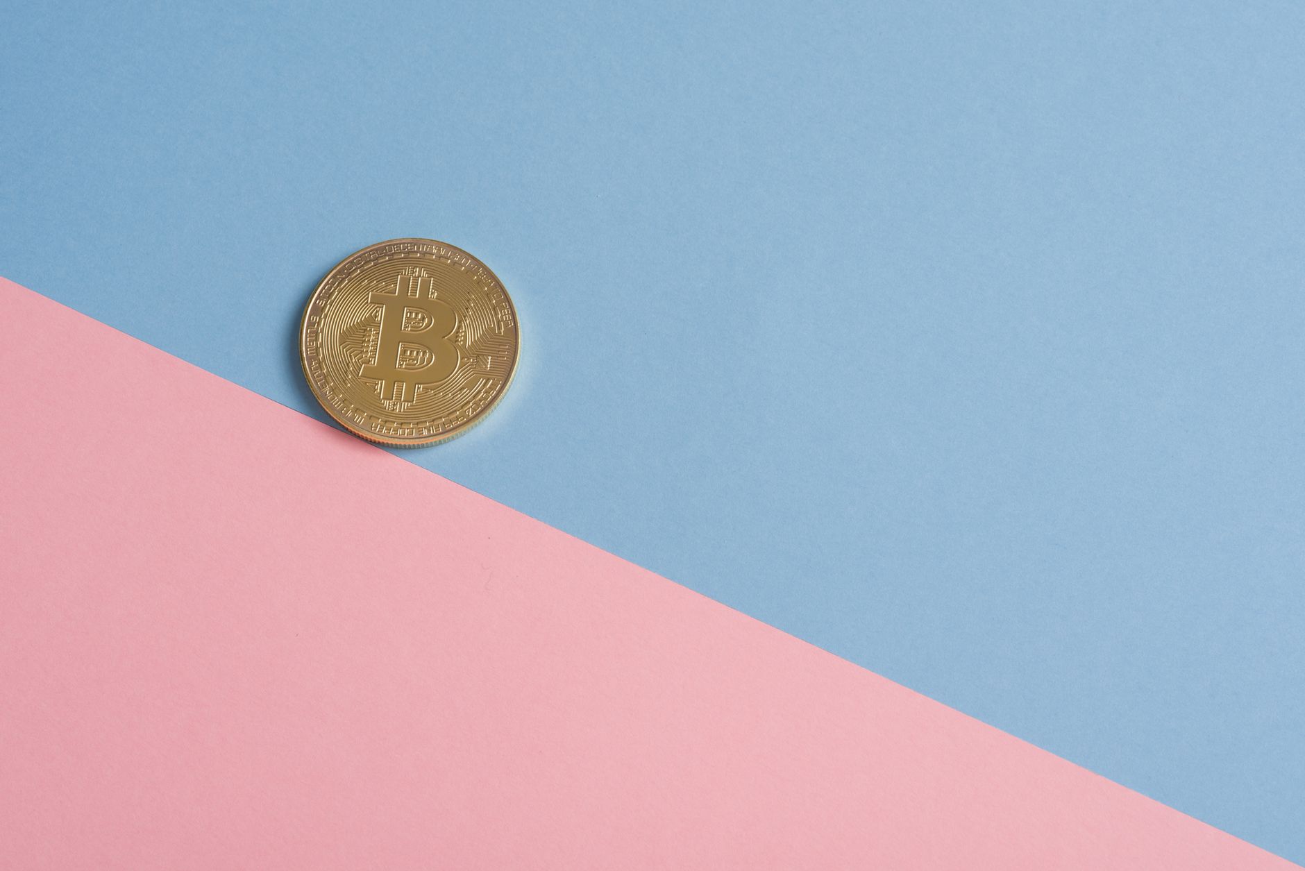 A single gold Bitcoin on a minimal pastel blue and pink background.
