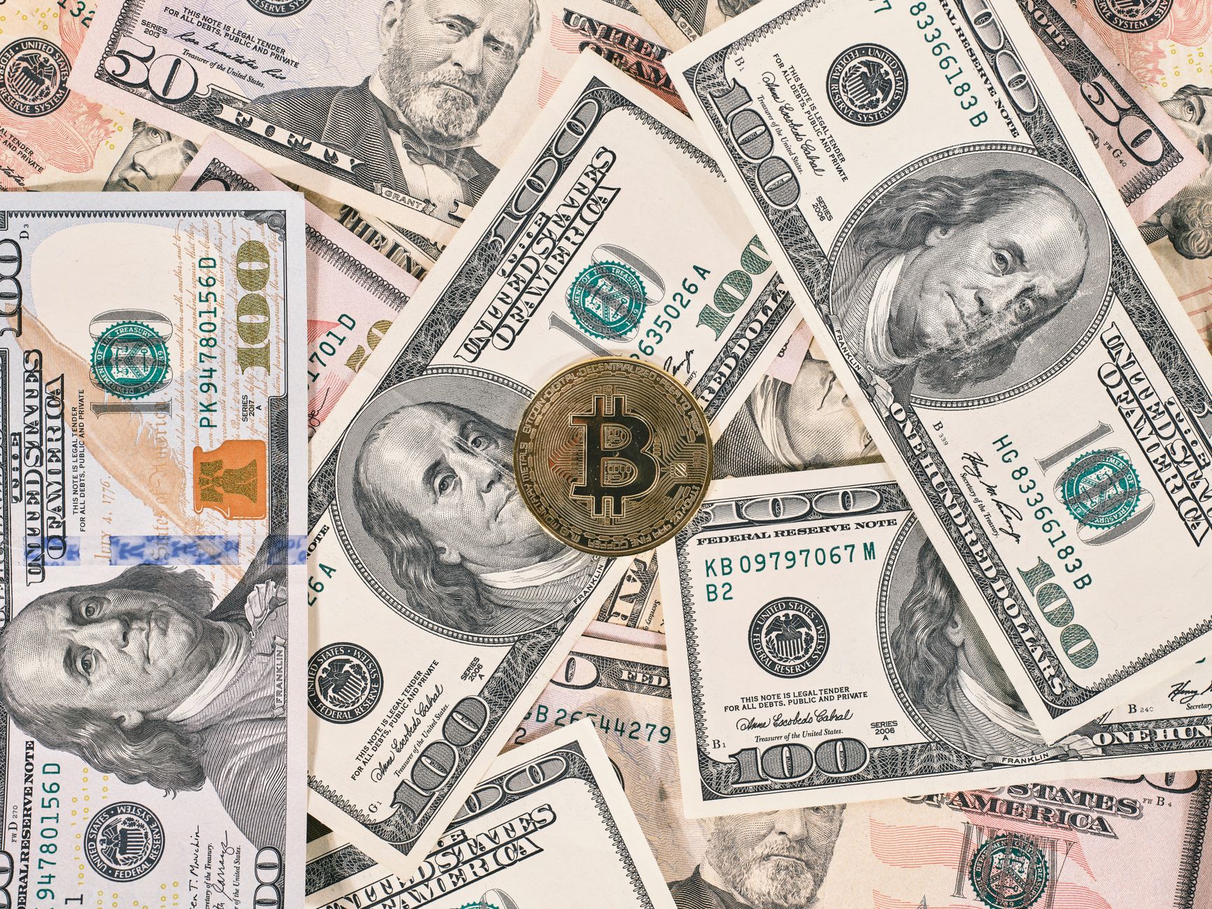 Bitcoin coin resting on a background of various US dollar bills, symbolizing the contrast between traditional and digital currency.