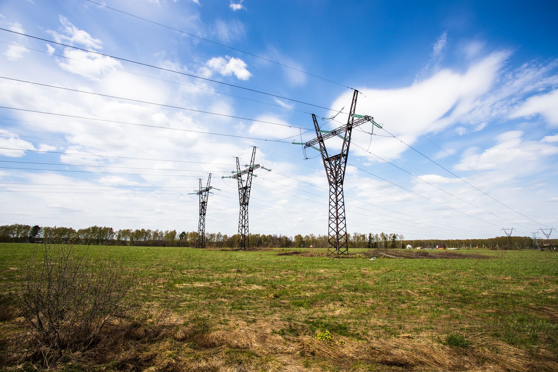 Scenic view of power lines crossing a green field under a bright blue sky.