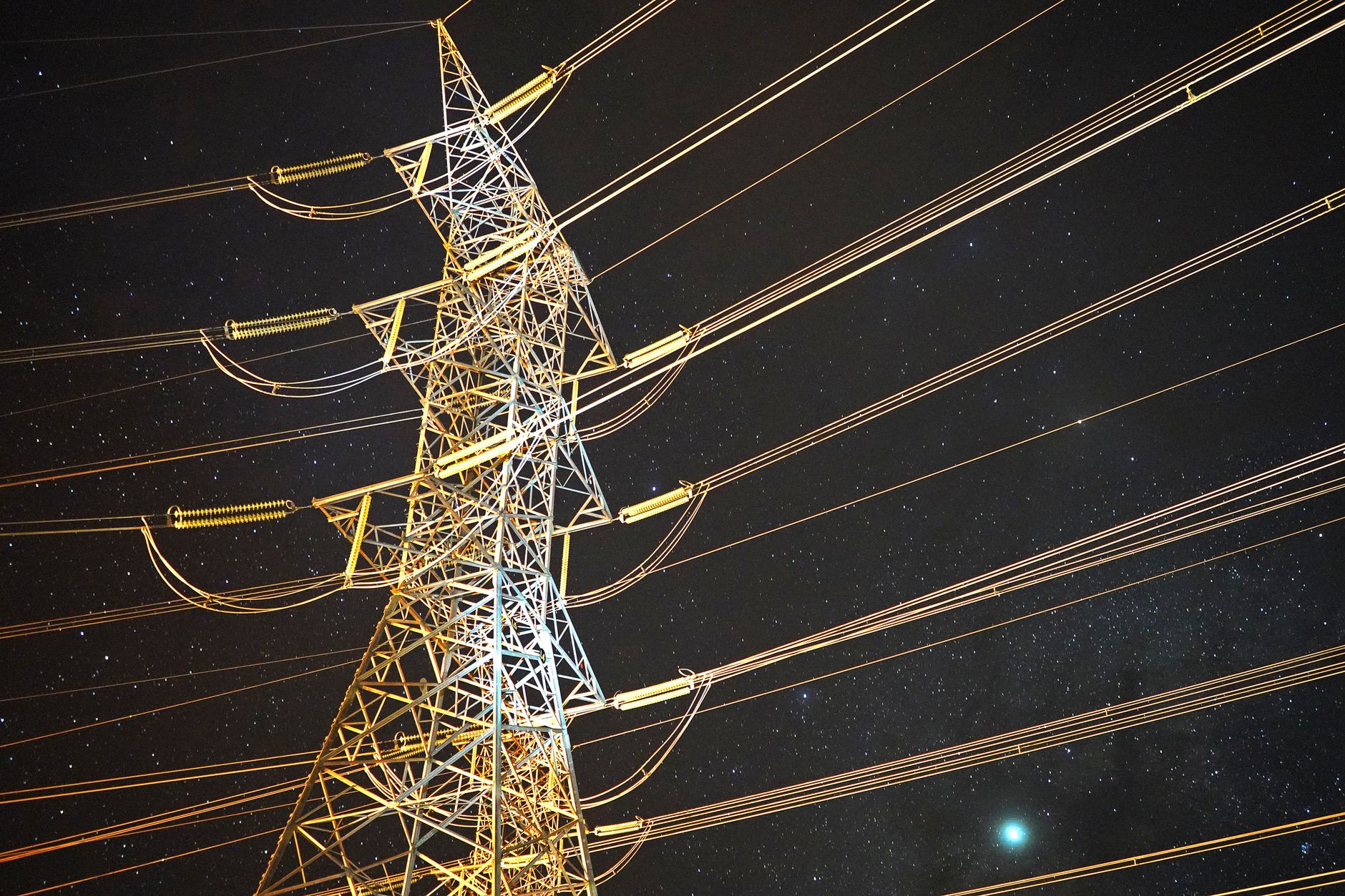Illuminated power tower against a starry night sky, showcasing energy infrastructure.