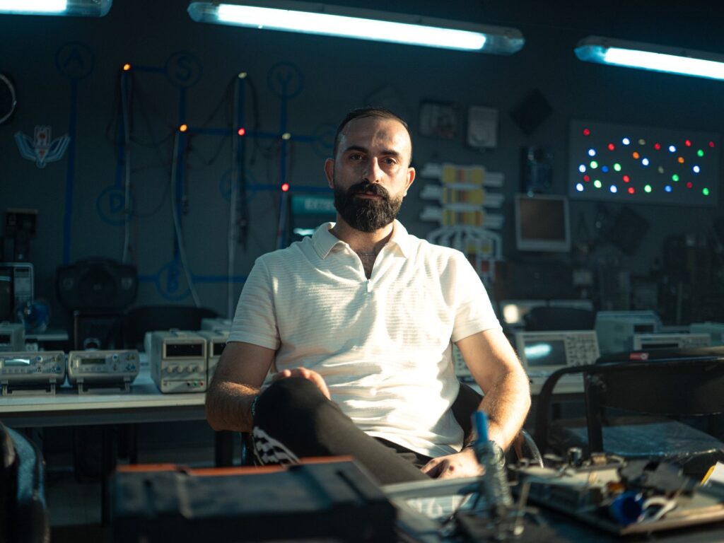 Portrait of a man in a technology lab surrounded by electronic equipment.