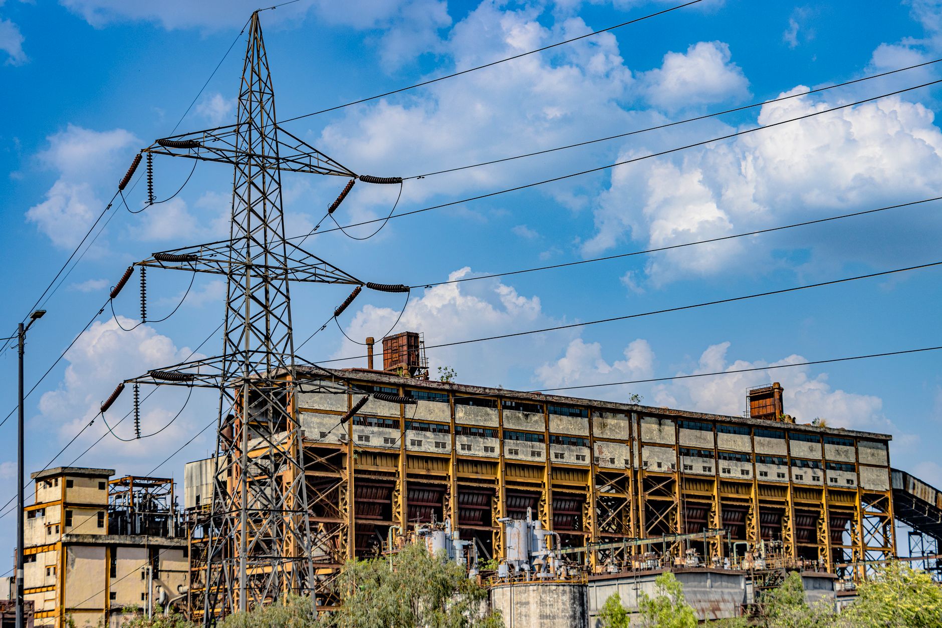 Photograph of an abandoned industrial building with a power line tower against a blue sky.