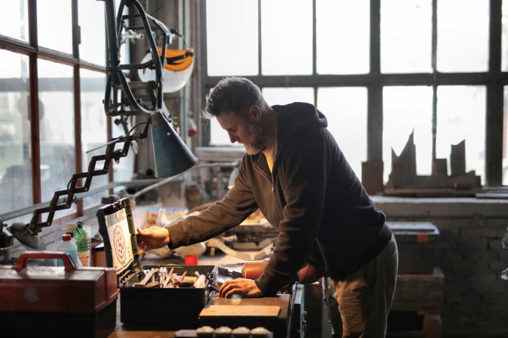 A male craftsman focuses on his work in a sunlit industrial workshop, using tools from a nearby toolbox.