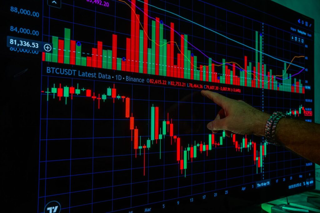A close-up of a hand pointing at cryptocurrency charts on a monitor, indicating market analysis.
