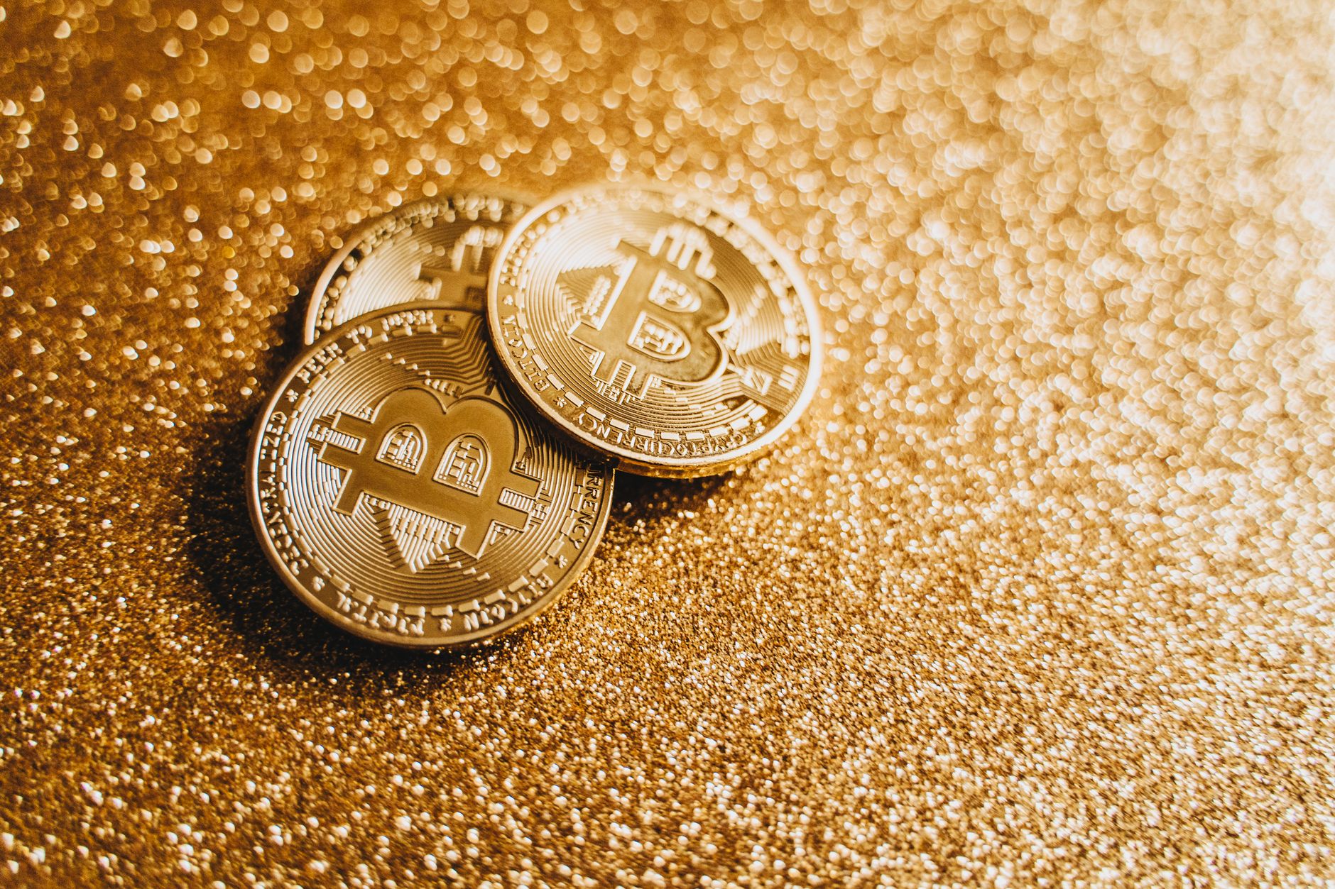 Closeup of three Bitcoin coins on a shimmering gold glitter background, symbolizing digital wealth.