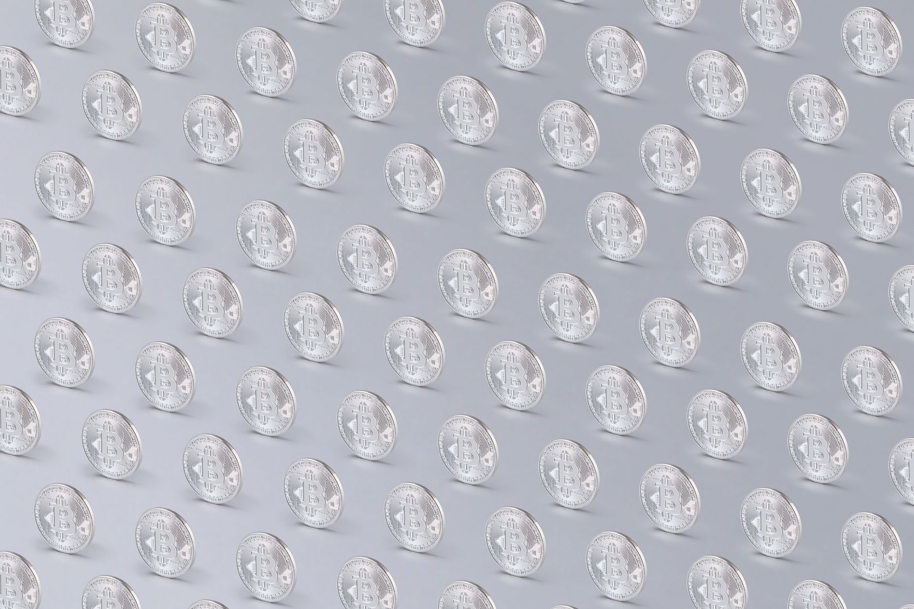 Array of silver Bitcoin coins arranged in a regular pattern over a light background.