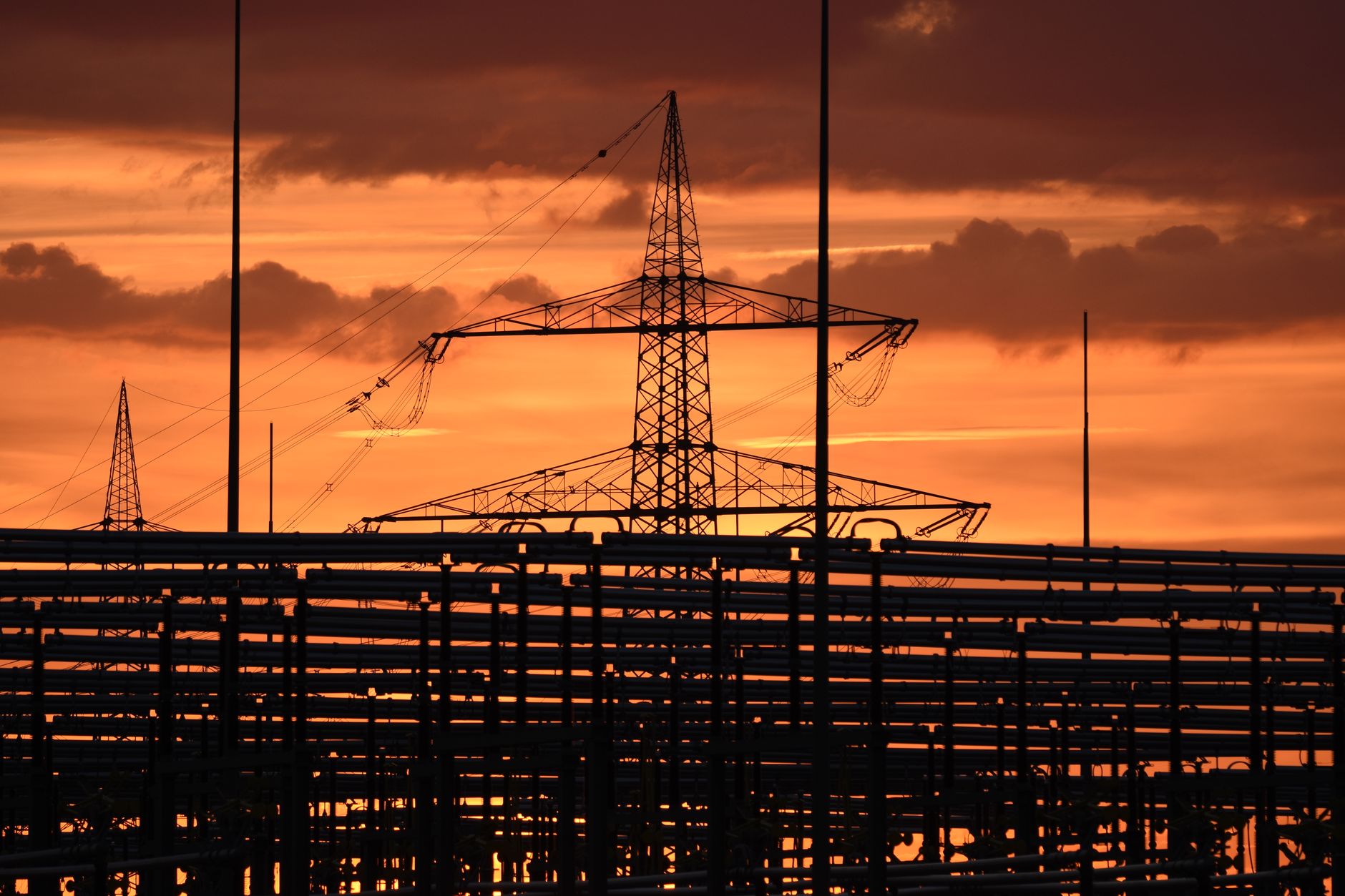Silhouetted electric tower against vivid sunset sky, highlighting urban infrastructure.