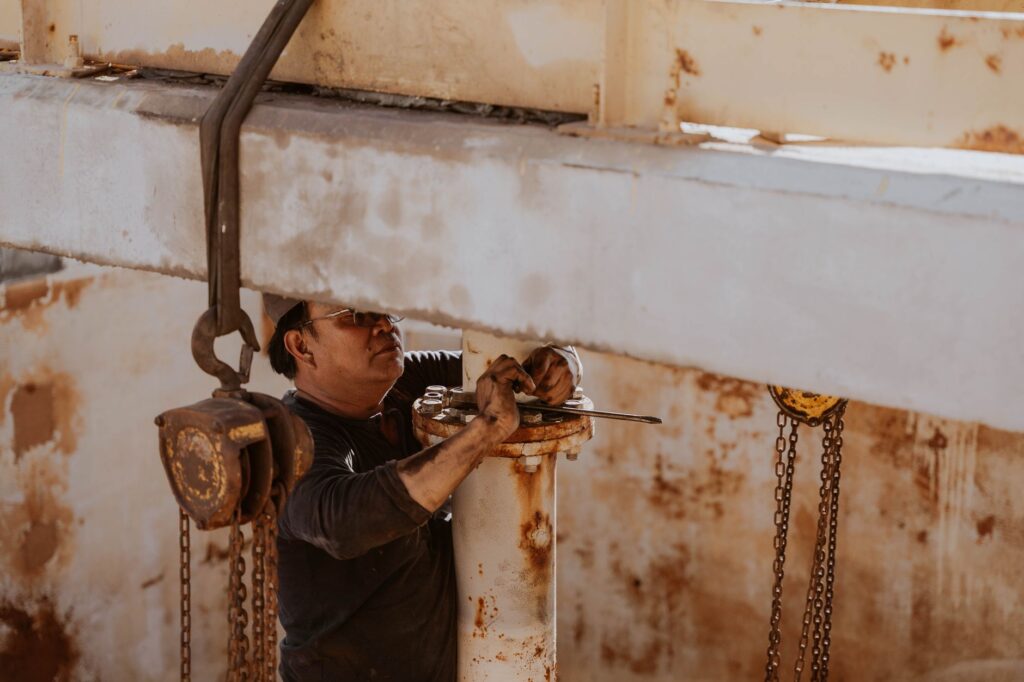 A worker in Libya repairs industrial machinery outdoors on a sunny day.