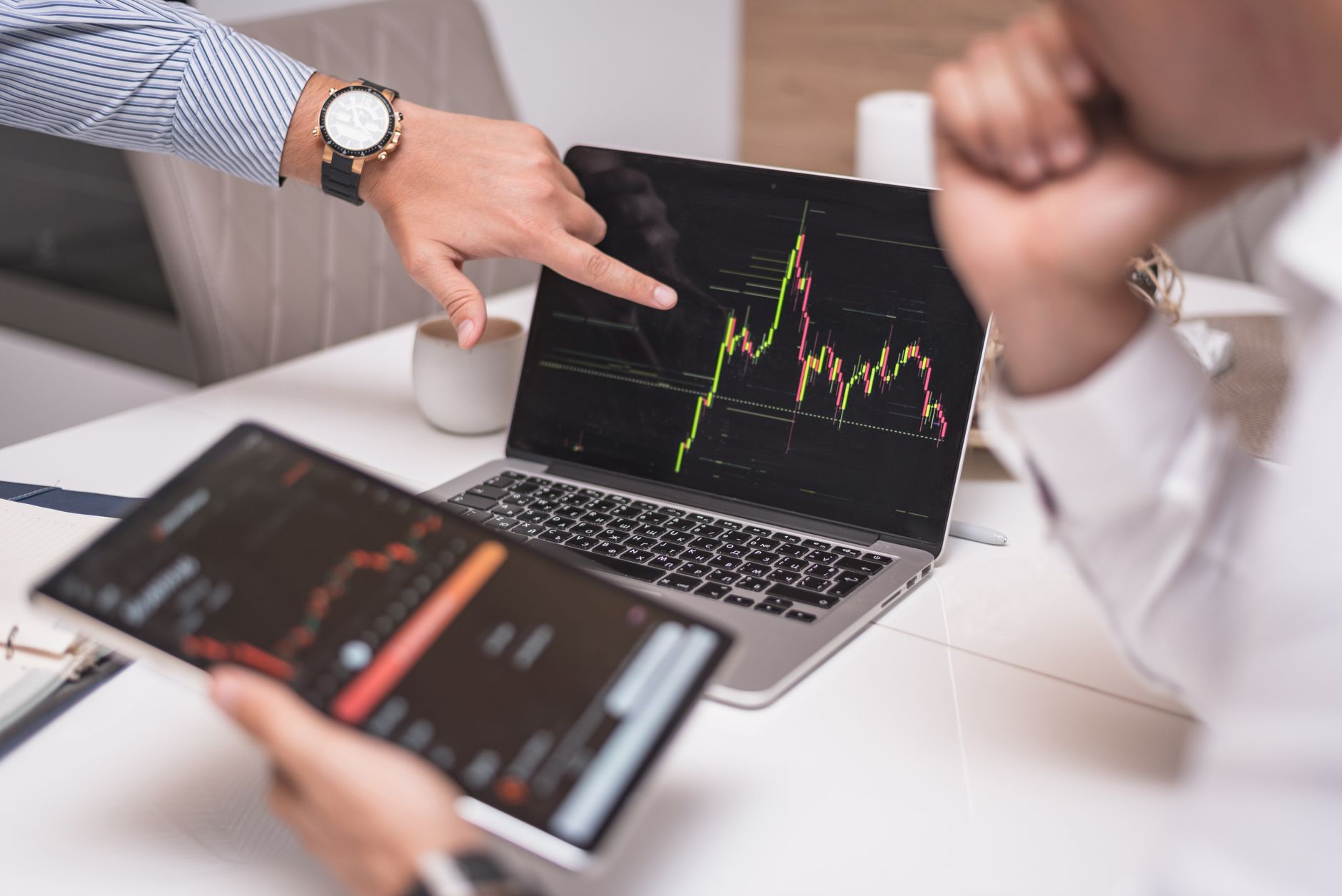 Business professionals analyzing cryptocurrency market trends on laptop and tablet.