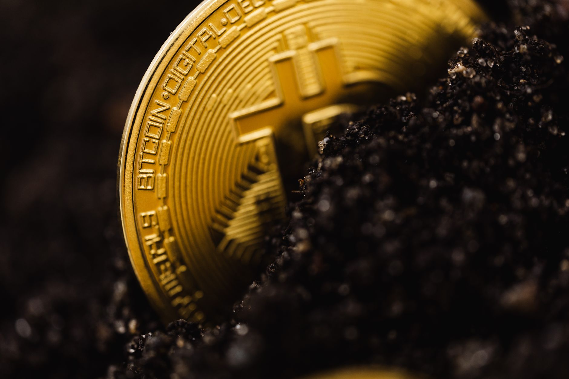 A close-up shot of a Bitcoin partially buried in soil, symbolizing digital currency growth.