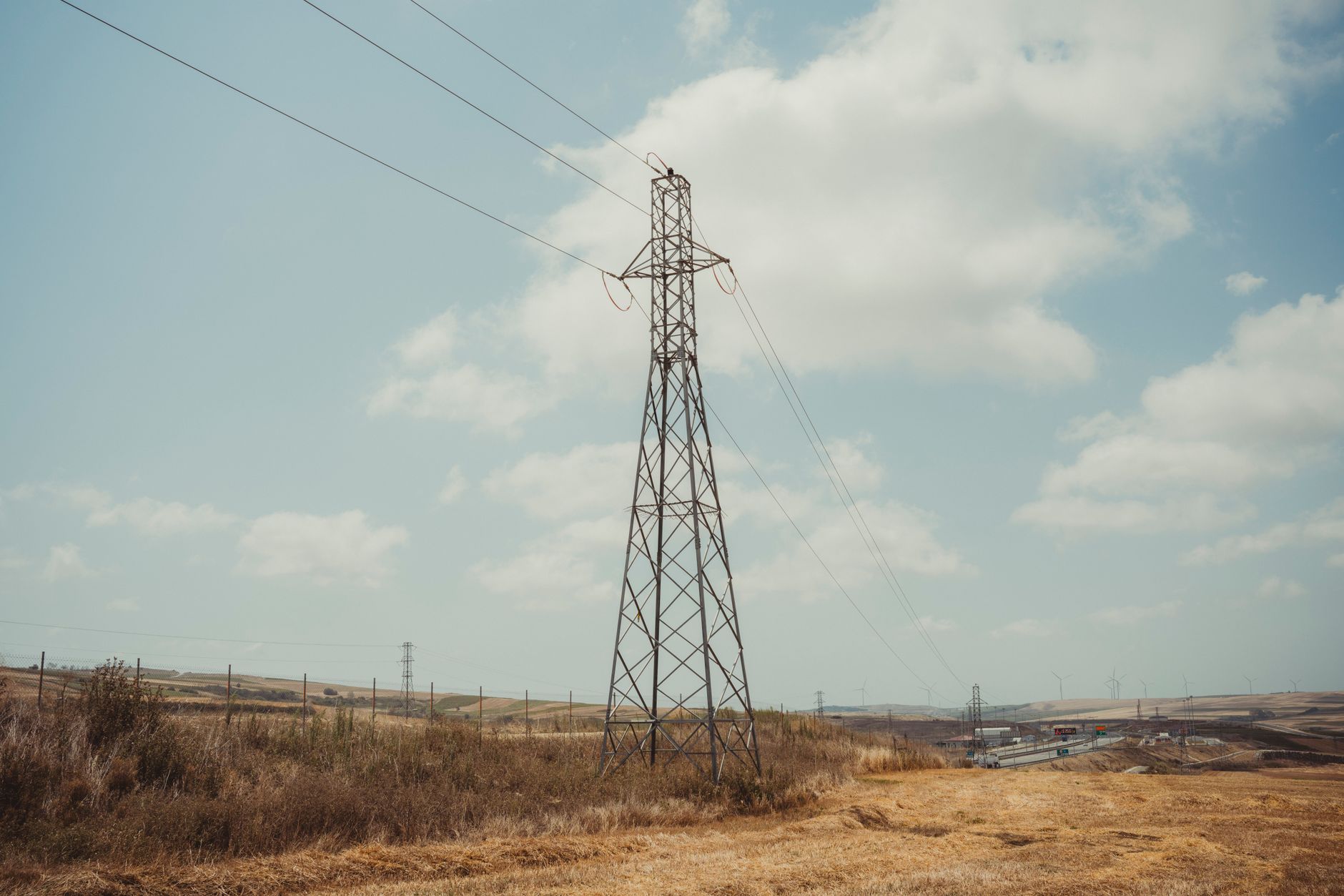 High voltage pylon in a countryside landscape under a blue sky with clouds.
