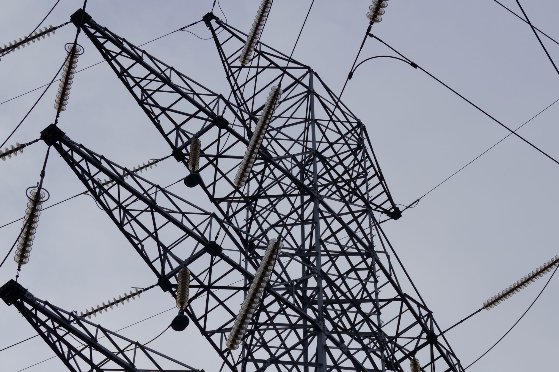 Low angle shot of a metal power transmission tower with cables against a clear sky.