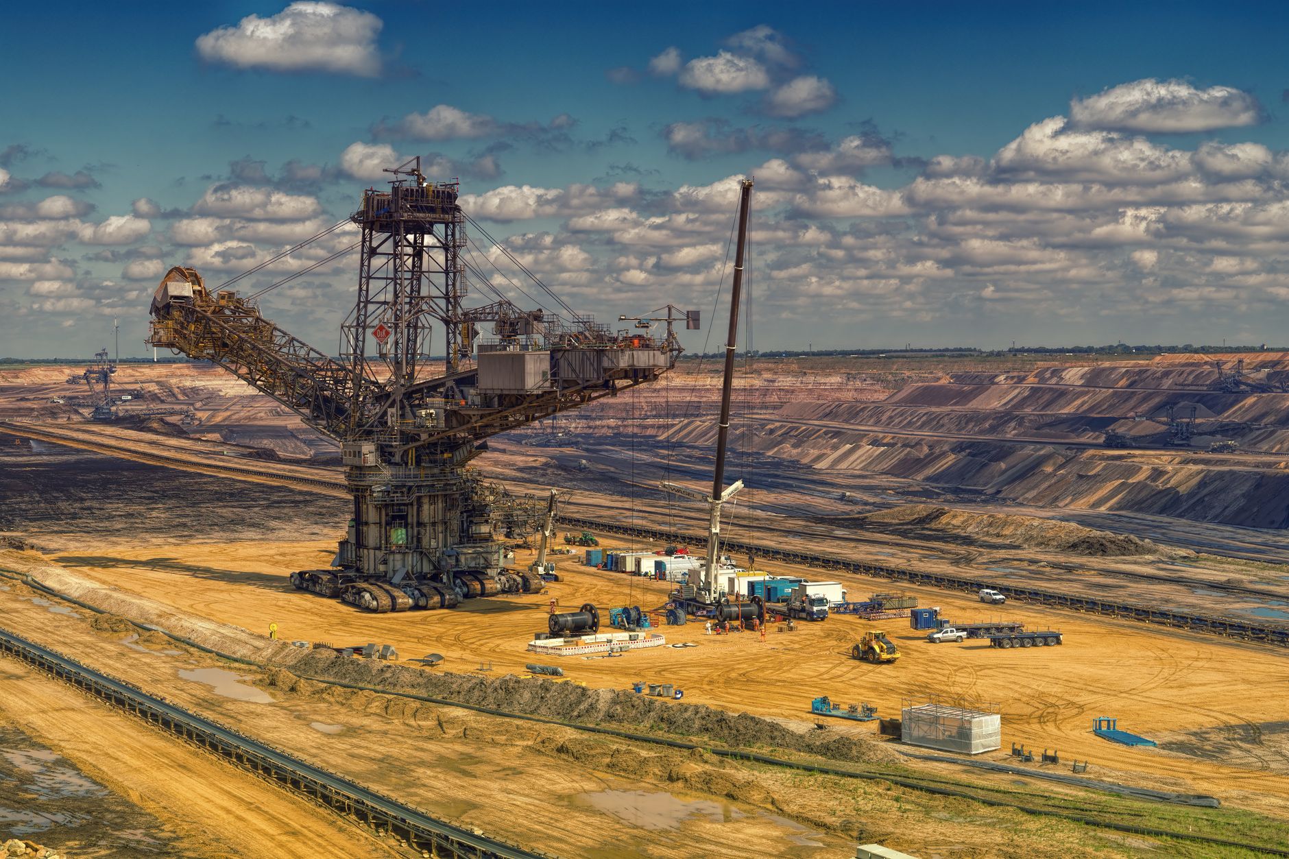 Aerial view of heavy machinery operating in a vast open-pit mine under a cloudy sky.