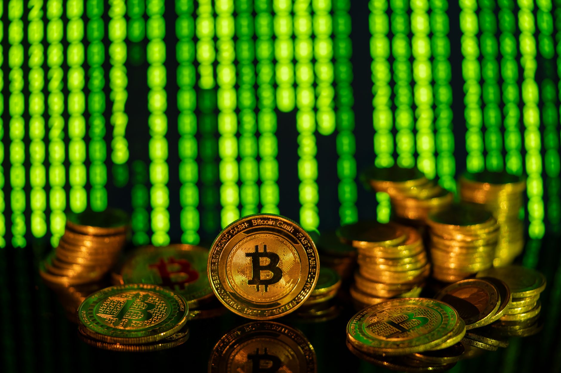 Stacks of golden bitcoins in front of a digital matrix, symbolizing cryptocurrency and blockchain technology.
