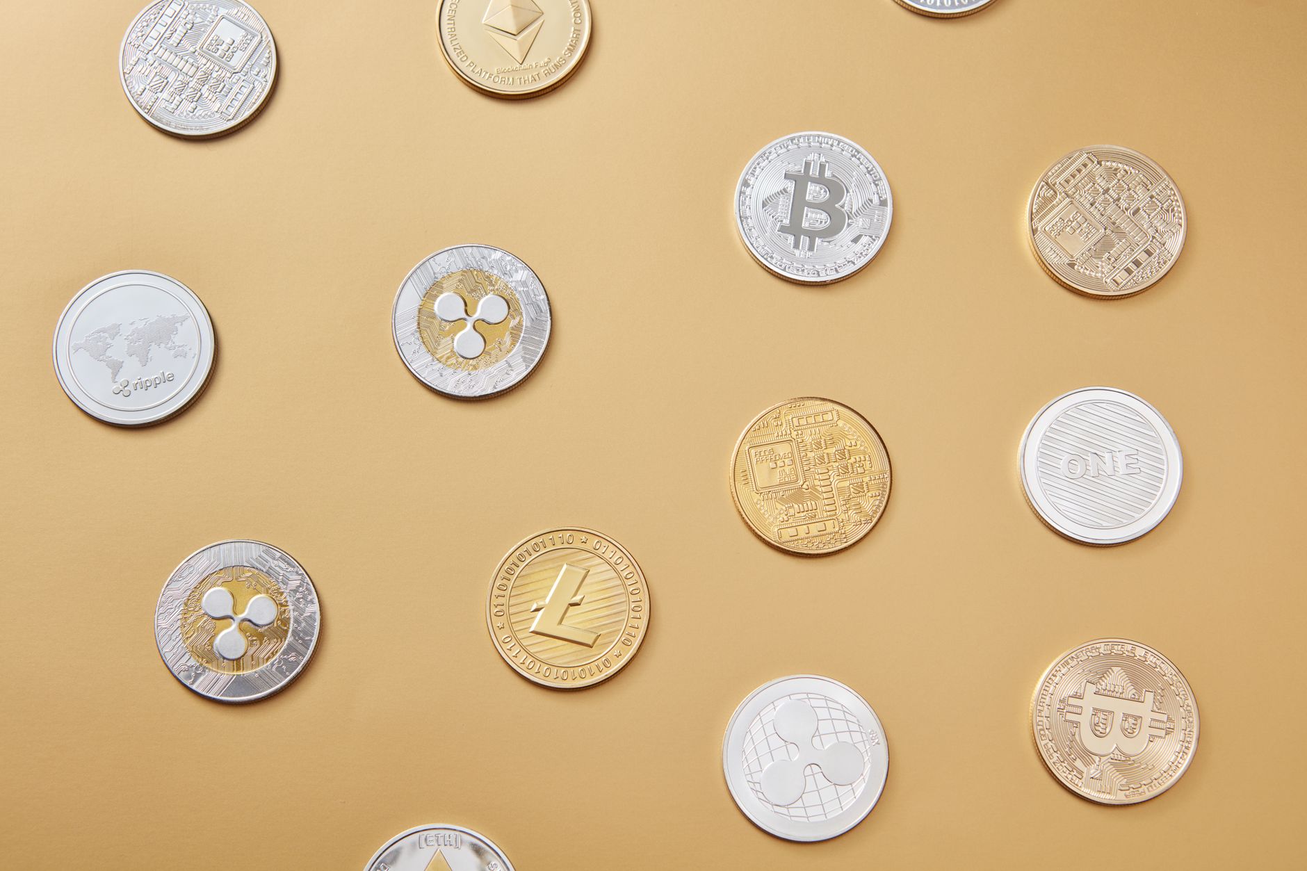 A flat lay of various cryptocurrency coins on a gold background, showcasing digital currency diversity.