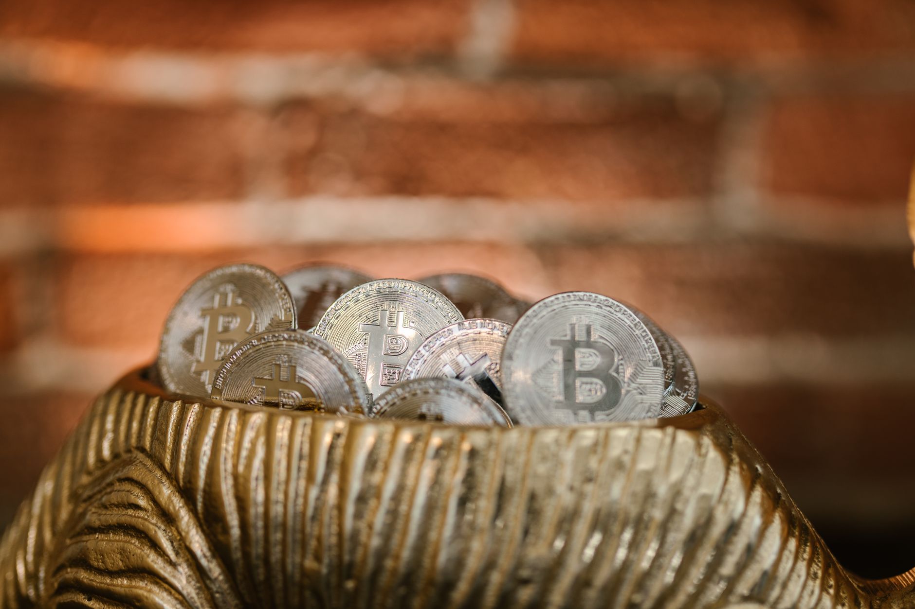 A collection of Bitcoin coins in a gold bowl with a textured brick background, signifying digital wealth.